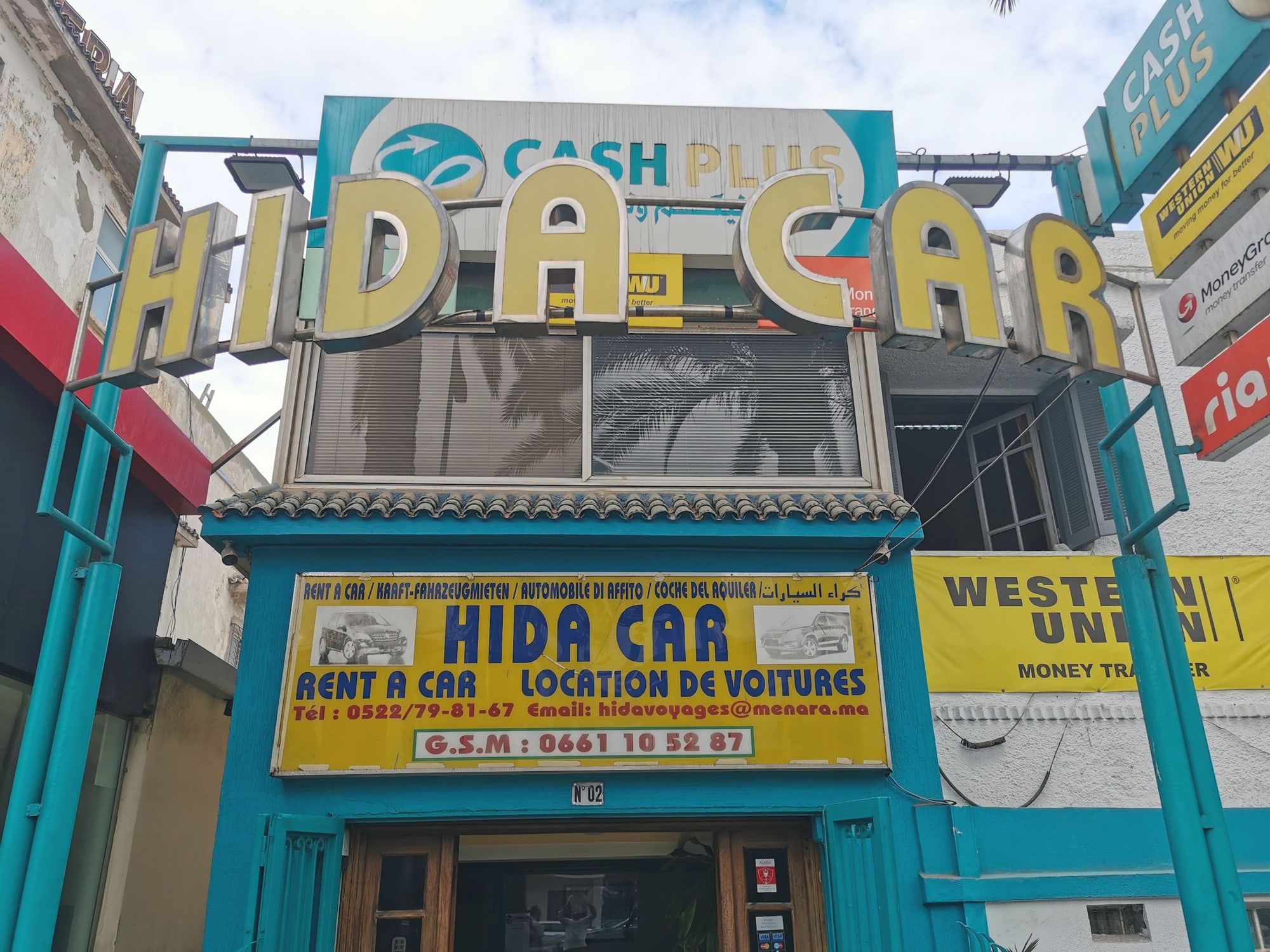 La devanture de jour : lettres jaunes HIDA CAR sur cadre turquoise, enseigne en six langues, N°02